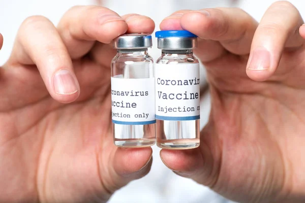 Vista de cerca de frascos con vacuna contra el coronavirus en manos de un médico borroso aislado en blanco — Stock Photo