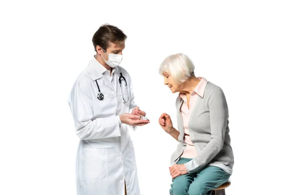 Médico con máscara médica que sostiene la vacuna cerca del paciente anciano aislado en blanco - foto de stock