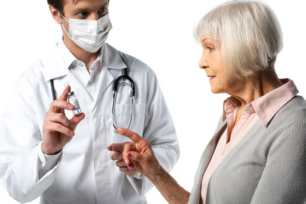 Старший пацієнт вказує на вакцину поблизу лікаря в медичній масці ізольовано на білому — стокове фото