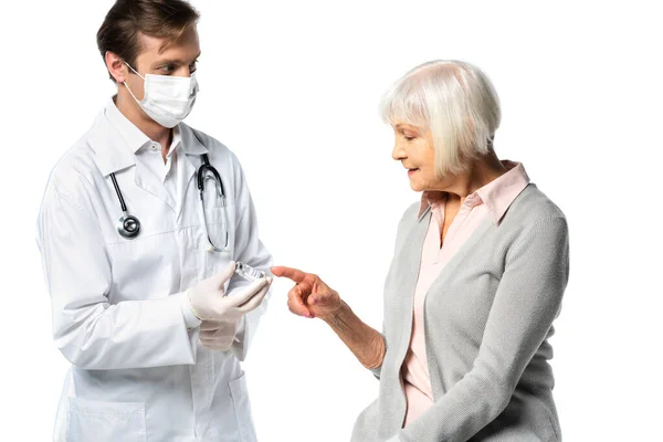 Paciente anciano señalando frasco con vacuna en la mano del médico en máscara protectora aislada en blanco - foto de stock