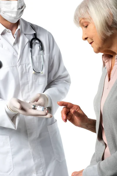 Paciente anciano señalando vacuna en mano del médico en máscara médica y guantes de látex aislados en blanco - foto de stock