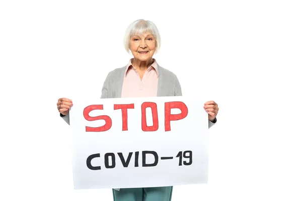 Mujer mayor sonriendo mientras sostiene la pancarta con las letras stop covid-2019 aisladas en blanco - foto de stock