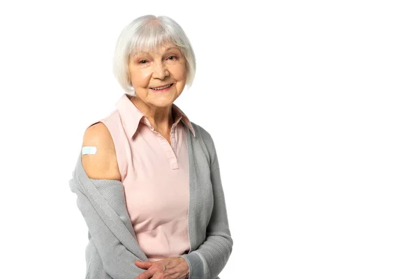 Positive elderly woman with adhesive plaster on arm looking at camera isolated on white — Stock Photo