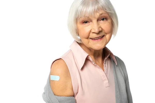 Ältere Frau mit Klebepflaster am Arm blickt isoliert auf weiße Kamera — Stockfoto