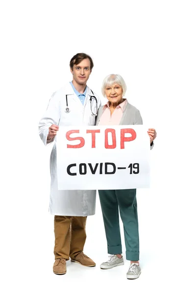 Senor paciente sonriendo mientras sostiene la pancarta con la letra stop covid-2019 cerca del médico sobre fondo blanco - foto de stock