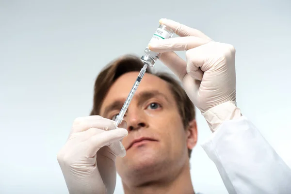 Visão de baixo ângulo do médico preparando a vacina em seringa isolada em cinza — Fotografia de Stock