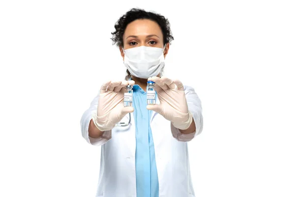 Pots avec vaccin dans les mains du médecin afro-américain en masque médical sur fond flou isolé sur blanc — Photo de stock