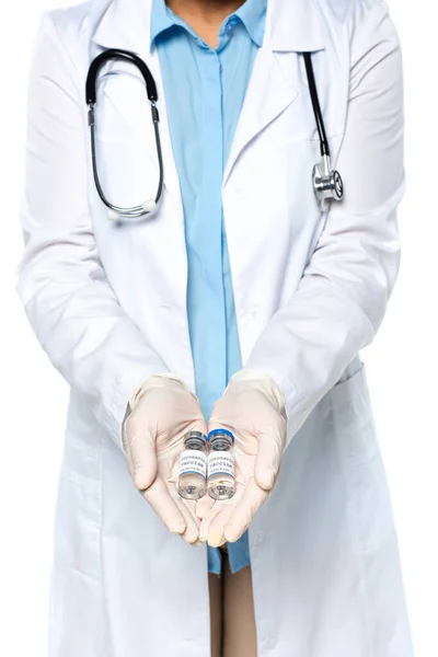 Vista recortada del médico con guantes de látex sosteniendo frascos con vacuna aislada en blanco - foto de stock