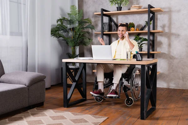 Joyeux homme handicapé gestuelle tout en parlant sur smartphone au bureau à la maison — Photo de stock