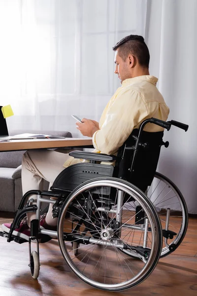 Behinderter Mann im Rollstuhl sendet während der Arbeit zu Hause Nachrichten auf dem Smartphone — Stockfoto