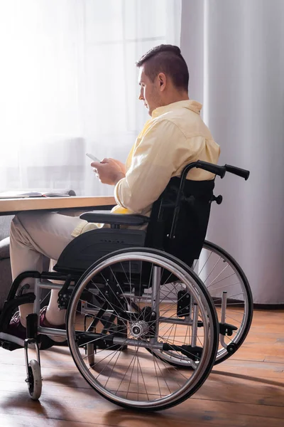 Homem em mensagens de cadeira de rodas no telefone celular enquanto trabalhava no escritório — Fotografia de Stock