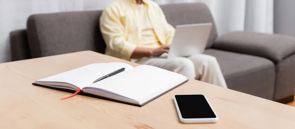 Messa a fuoco selettiva di notebook e smartphone con schermo vuoto vicino a freelance su sfondo sfocato, banner — Foto stock