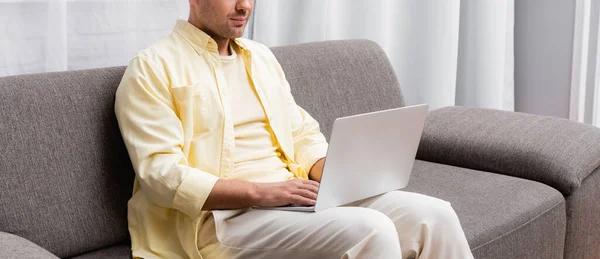 Teilansicht des Freiberuflers auf der Couch sitzend und auf Laptop tippend, Banner — Stockfoto