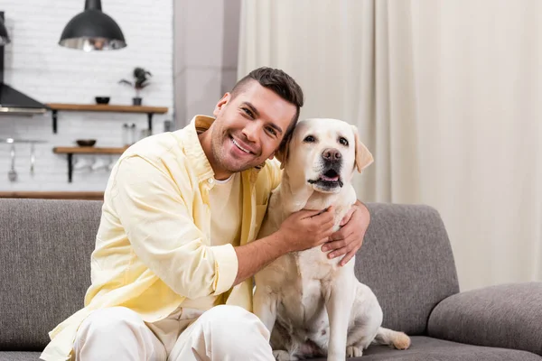 Uomo felice sorridente alla macchina fotografica mentre abbraccia cane labrador — Foto stock