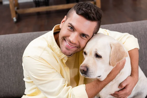 Jovem abraçando cão labrador enquanto sorrindo para a câmera — Fotografia de Stock