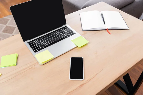 High angle view of mobile phone and laptop with blank screen near sticky notes and notebook on desk — Stock Photo