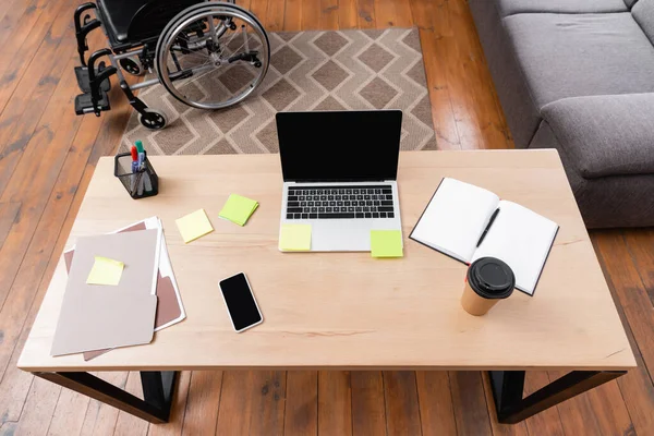 High angle view of desk with gadgets, documents and takeaway drink near wheelchair — Stock Photo
