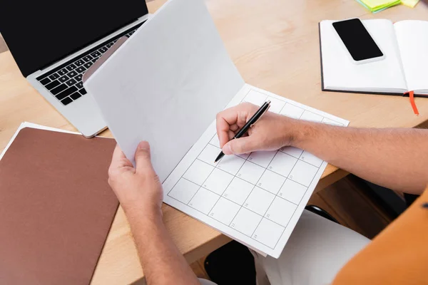 Vista parcial del freelancer escribiendo en el planificador diario mientras trabaja en casa - foto de stock