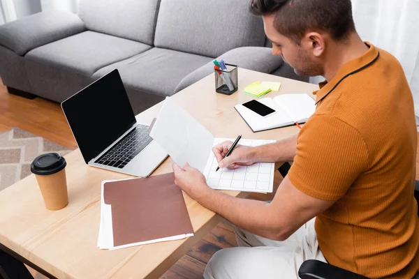 Vue grand angle de l'écriture pigiste dans le planificateur quotidien près d'un ordinateur portable avec écran blanc — Stock Photo