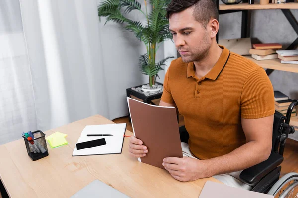 Junger behinderter Mann hält Dokumente während er im Home Office sitzt — Stockfoto