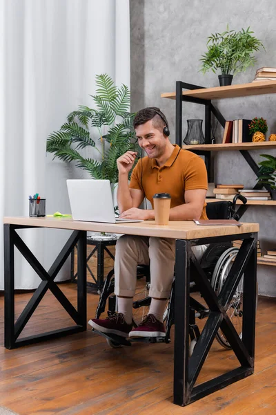 Веселый, инвалид в гарнитуре работает в домашнем офисе рядом с ноутбуком — стоковое фото