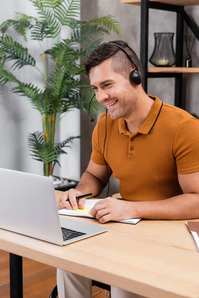 Homem com deficiência olhando para laptop enquanto trabalhava em headset em home office — Fotografia de Stock