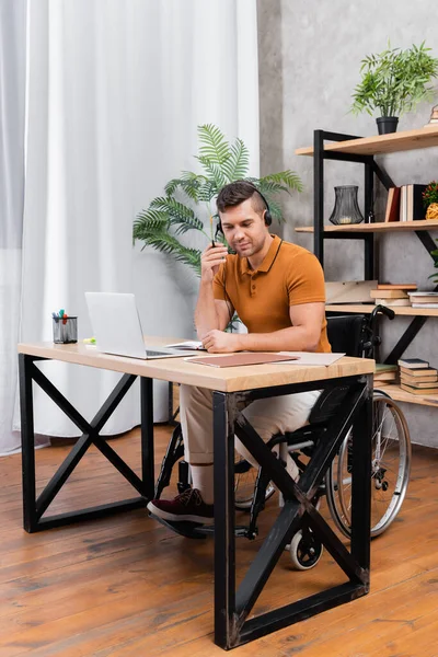 Giovane handicappato in auricolare che lavora in ufficio vicino al computer portatile — Foto stock