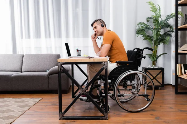 Инвалид в наушниках, работающий возле ноутбука дома — стоковое фото