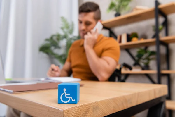 Selective focus of cube with disability sign near man talking on smartphone on blurred background — Stock Photo