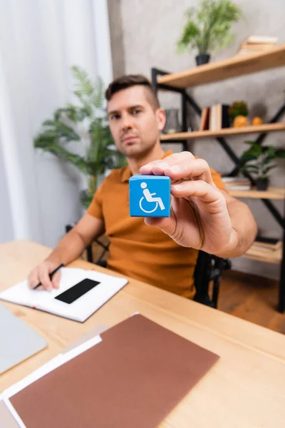 Selektiver Würfelfokus mit Behinderungszeichen in der Hand eines Freiberuflers, der zu Hause arbeitet — Stockfoto