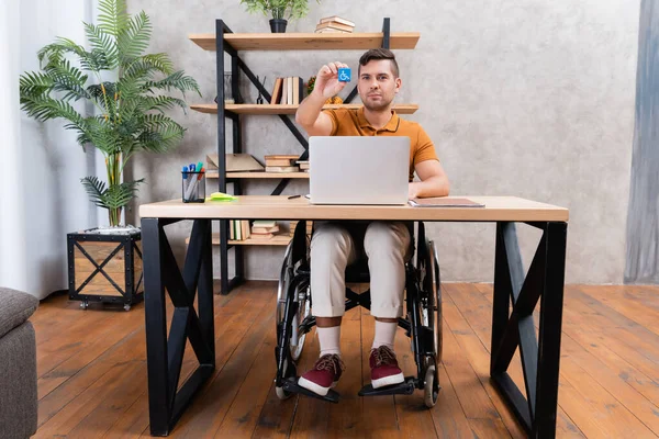 Homme handicapé montrant cube avec symbole de handicap tout en travaillant au bureau à domicile — Photo de stock