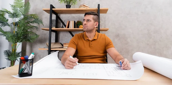 Nachdenklicher Ingenieur schaut weg, während er in der Nähe von Bauplänen zu Hause arbeitet, Banner — Stockfoto