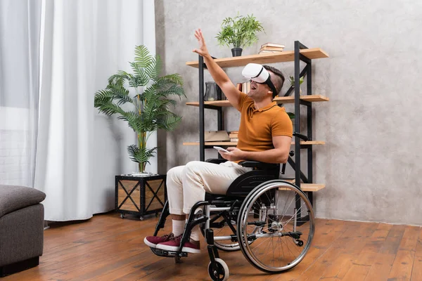 Homem deficiente surpreso em vr fone de ouvido sentado em cadeira de rodas com a mão estendida — Fotografia de Stock