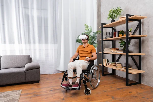 Deficiente homem jogos no vr fone de ouvido enquanto sentado em cadeira de rodas em casa — Fotografia de Stock