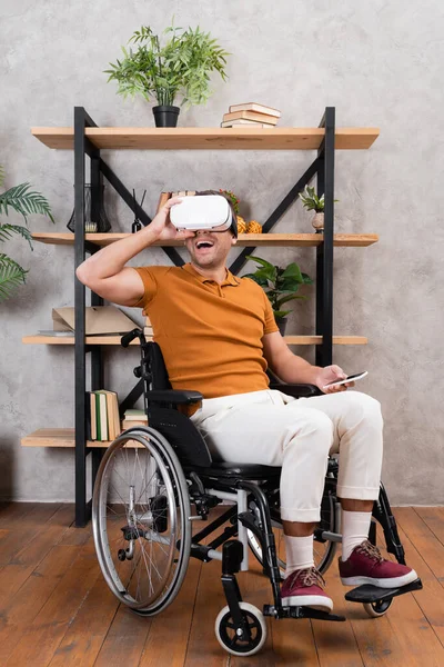 Excité homme réglage vr casque tout en jouant en fauteuil roulant à la maison — Photo de stock