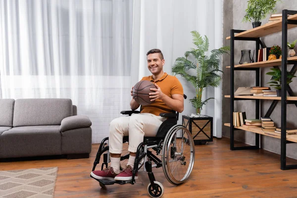 Deficiente homem em cadeira de rodas segurando basquete e sorrindo para a câmera — Fotografia de Stock