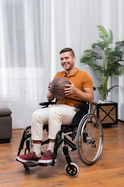 Веселый инвалид держит баскетбол, сидя в инвалидной коляске — стоковое фото