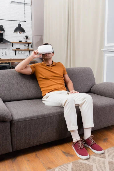 Мужчина настраивает гарнитуру VR, играя на диване дома — стоковое фото