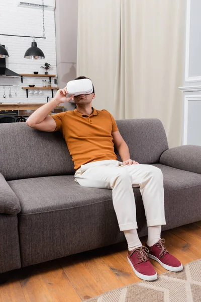 Homem ajustando vr fone de ouvido enquanto joga no sofá em casa — Fotografia de Stock