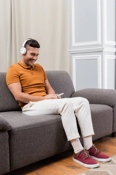 Pleased man chatting on cellphone while listening music in wireless headphones — Stock Photo