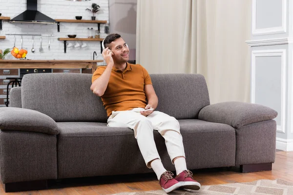 Joyful man holding smartphone while listening music in headphones on sofa — Stock Photo