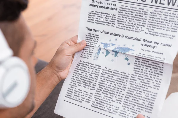 Cropped view of man in headphones reading newspaper on blurred foreground — Stock Photo