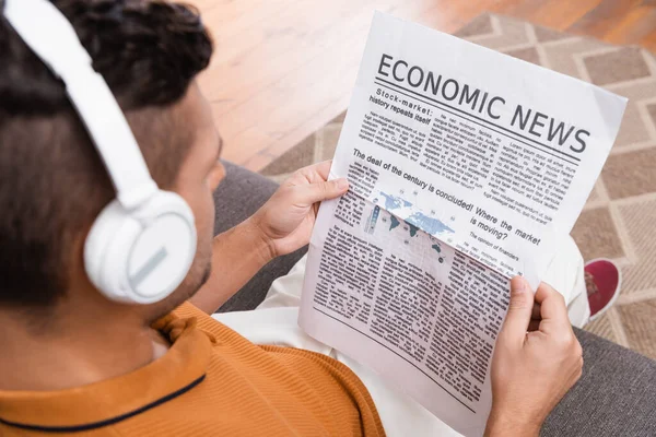 Vista aérea del hombre en auriculares que leen noticias económicas en primer plano borroso - foto de stock