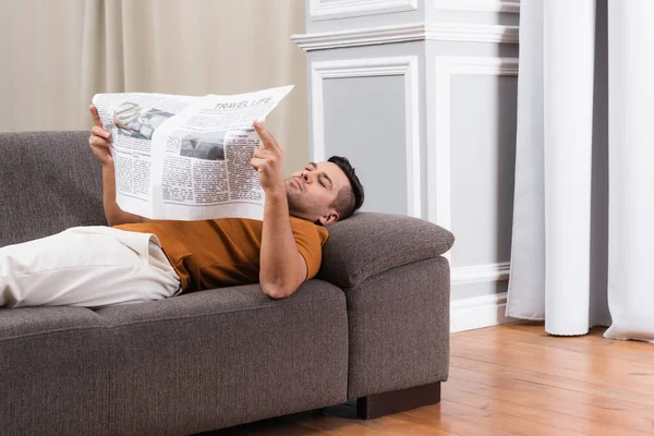 Uomo sdraiato sul divano e leggere giornali a casa — Foto stock