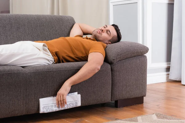 Jeune homme dormant sur le canapé tout en tenant journal — Photo de stock