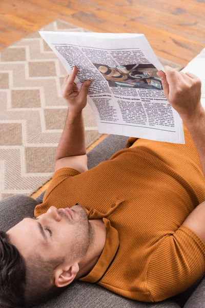 Вид сверху на молодого человека, читающего газету лежа на диване — стоковое фото