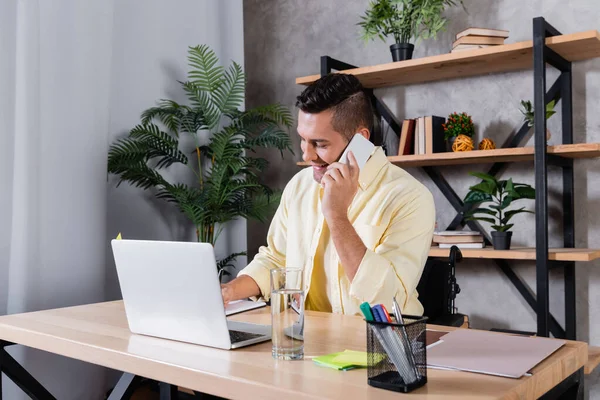 Інвалідний чоловік дзвонить на мобільний телефон під час роботи вдома біля ноутбука — стокове фото