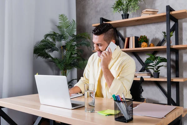 Uomo handicappato che chiama sul telefono cellulare mentre lavora a casa vicino al computer portatile — Foto stock