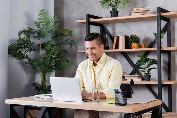 Homme handicapé souriant en tapant sur ordinateur portable à la maison — Photo de stock