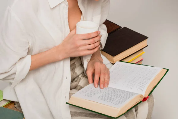 Обрезанный вид женщины, читающей книгу и держа чашку кофе изолированы на серый — стоковое фото